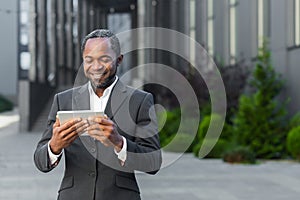 African american man in business suit outside office building watching online video with using app on tablet computer