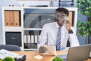 African american man business worker talking on smartphone reading notebook at office