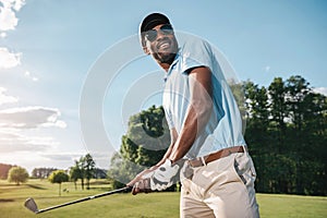 African american man in cap and sunglasses holding club and playing golf