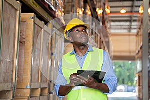 African american man checking stock working in a warehouse. A man wearing helmet and reflective jacket working in a warehouse.