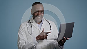 African american man doctor therapist ethnic male surgeon in white coat in blue background studio working on laptop