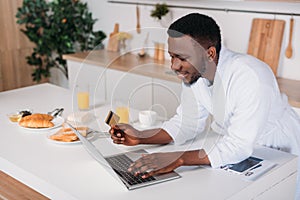 African american man doing online shopping and standing with credit card