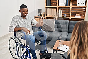 African american man doing therapy sitting on wheelchair smiling looking to the camera showing fingers doing victory sign