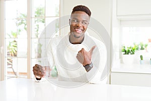 African american man driking a fresh glass of water pointing and showing with thumb up to the side with happy face smiling