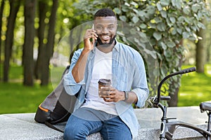 African American Man Drinking Coffee In Park And Talking On Cellphone