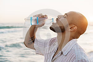 African american man drinking water from the bottle on beach