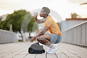 An African American man drinking water on a bridge. A man taking a break from exercising drinking from a bottle. A