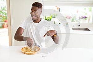 African american man eating cheese pizza at home very happy pointing with hand and finger