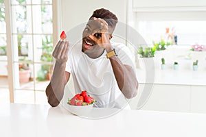 African american man eating fresh healthy strawberries with happy face smiling doing ok sign with hand on eye looking through