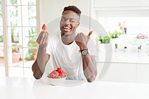 African american man eating fresh healthy strawberries pointing and showing with thumb up to the side with happy face smiling