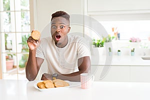 African american man eating healthy whole grain biscuit scared in shock with a surprise face, afraid and excited with fear