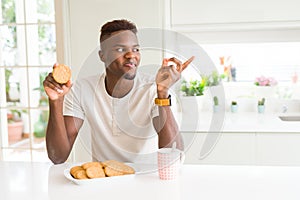 African american man eating healthy whole grain biscuit very happy pointing with hand and finger to the side