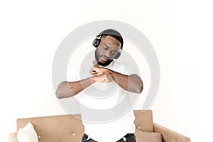 African American man enjoying music in wireless big headphones and dancing at home. Relax alone