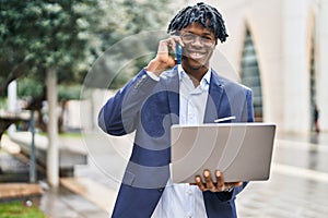 African american man executive using laptop and talking on the smartphone at park