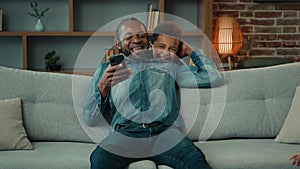 African American man father using mobile phone browsing smartphone at home couch sofa two little children kids sons boys