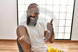 African american man getting vaccine showing arm with band aid smiling happy and positive, thumb up doing excellent and approval