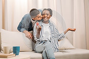 african american man gifting ring in heart shaped box to woman sitting on couch