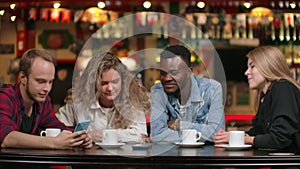 African-American man with a girl looking at a smartphone and talking while sitting in a coffee and drinking coffee