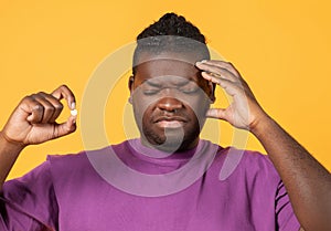 African american man having painful headache holding painkiller pill, studio