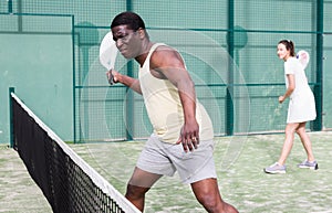 African american man and his female partner playing paddle tennis on padel court