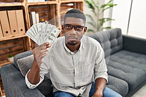 African american man holding dollars thinking attitude and sober expression looking self confident