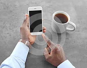 African-American man holding phone with blank screen in hand at table