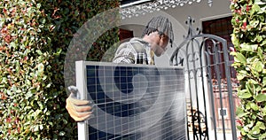 African american man holding photovoltaic panel entering property, slow motion