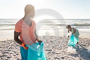 African american man holding plastic bag while looking at girlfriend collecting garbage from beach