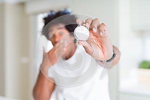 African American man holding stopwatch cover mouth with hand shocked with shame for mistake, expression of fear, scared in