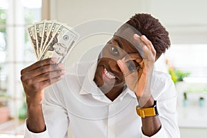 African american man holding twenty dollars bank notes with happy face smiling doing ok sign with hand on eye looking through