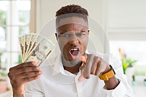 African american man holding twenty dollars bank notes pointing with finger to the camera and to you, hand sign, positive and