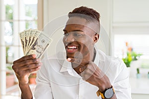 African american man holding twenty dollars bank notes very happy pointing with hand and finger
