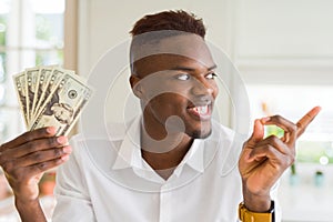 African american man holding twenty dollars bank notes very happy pointing with hand and finger to the side