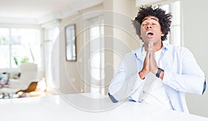 African American man at home begging and praying with hands together with hope expression on face very emotional and worried