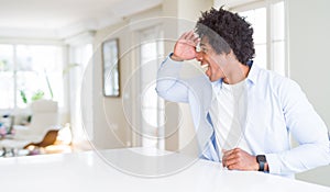 African American man at home very happy and smiling looking far away with hand over head