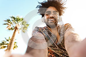 African american man listening music with headphones outdoor with palm trees in background - Summer lifestyle, travel and party photo