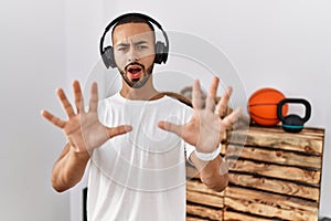 African american man listening to music using headphones at the gym afraid and terrified with fear expression stop gesture with