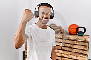 African american man listening to music using headphones at the gym angry and mad raising fist frustrated and furious while