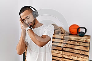 African american man listening to music using headphones at the gym sleeping tired dreaming and posing with hands together while