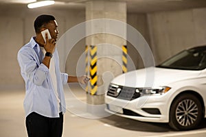 African american man locking his car with keys in underground parking while talking on the phone