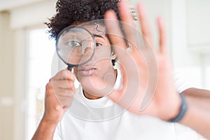 African American man looking through magnifying glass with open hand doing stop sign with serious and confident expression,