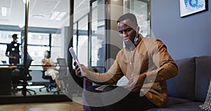 African american man with lowered face mask showing document while having video chat on digital tabl