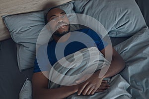 African American Man Lying In Bed Awake Having Insomnia Indoors