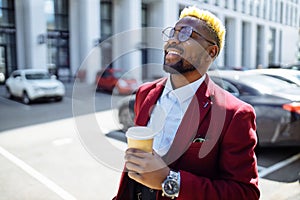 African american man in marsala jacket drinks coffee to go frop paper eco cup outdoor in centre office