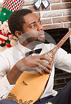 African American man with Musical instrument Dombra by fireplace. Christmas