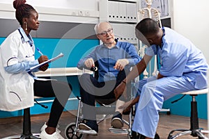 African american man nurse checking injured knee leg of sick senior patient