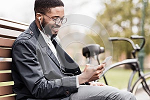 African-american man with phone sitting on bench near bicycle