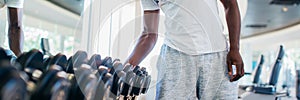 African American man picking up a dumbbell from the rack and looking outside at gym