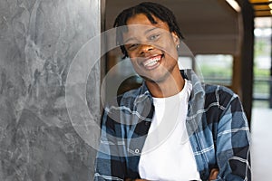 African American man in plaid shirt smiles, leaning on a wall in modern office