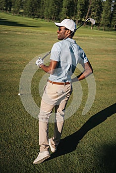 African american man playing golf with club and ball at green lawn